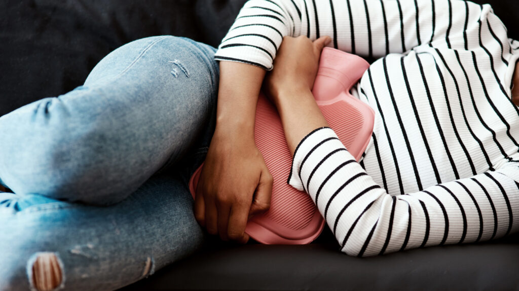 Cropped-shot-of-a-woman-holding-a-hot-water-bottle-against-her-stomach-on-the-sofa-at-home